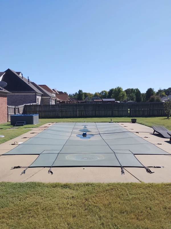 Mesh safety cover over a rectangular pool beside a lawn